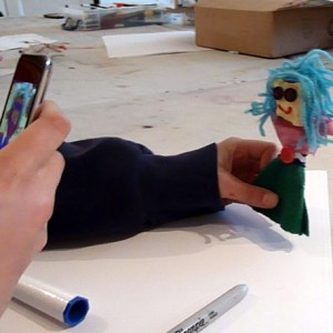 Nina takes a photo of her puppet on a devise