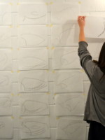 Libby placing her minimalised drawings on the wall as she completes them