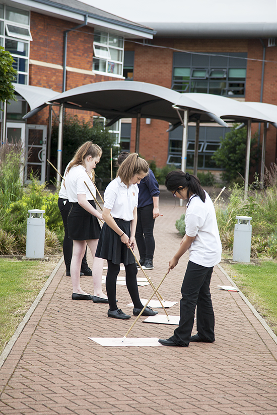 Students draw using compressed charcoal taped to long bamboo canes