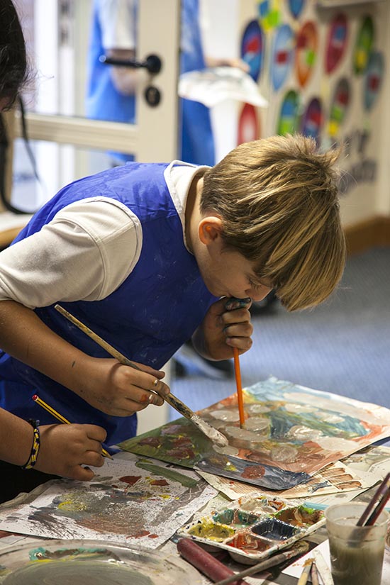 Pupil explores mark making by blowing paint across the paper with a straw