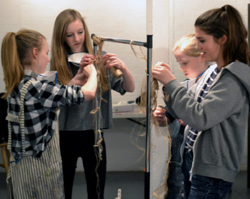 Two groups of students work with string, hanging it over a bar to create suspended sculptures