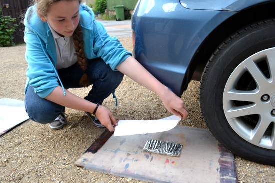 Student lays a piece of damp paper over her inked up plate on a drawing board sandwiched in plastic