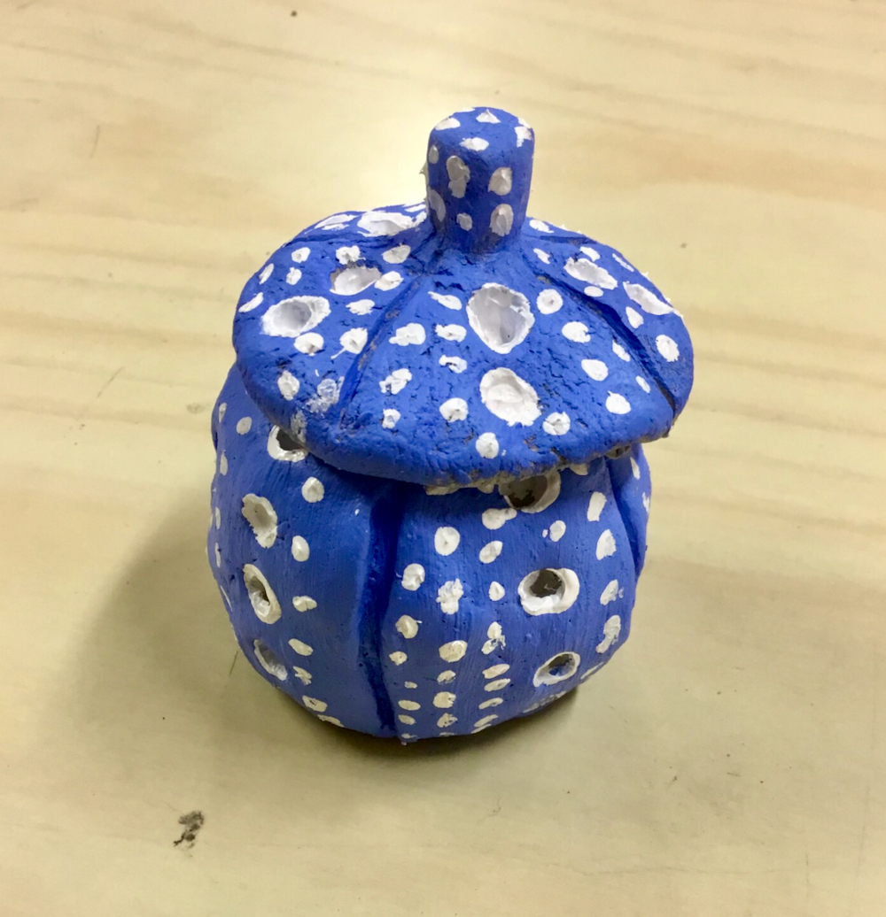 A blue pot with a lid painted with a shiny, light blue background decorated with white spots by a Year Six pupil