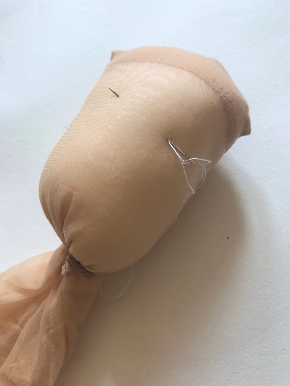 pushing a needle and thread through the stuffed head