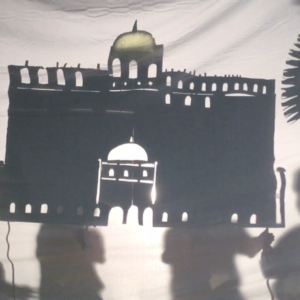 Holding up a large shadow puppet of a palace