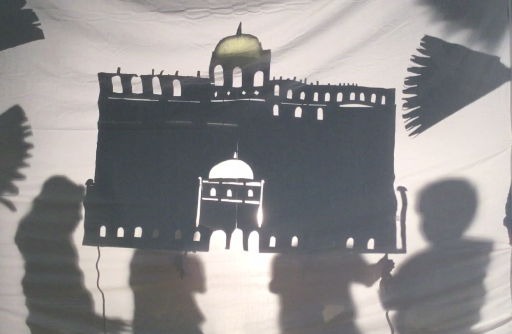 Holding up a large shadow puppet of a palace