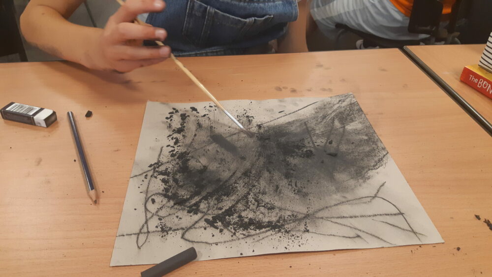 Using a dry paint brush to smudge charcoal into paper