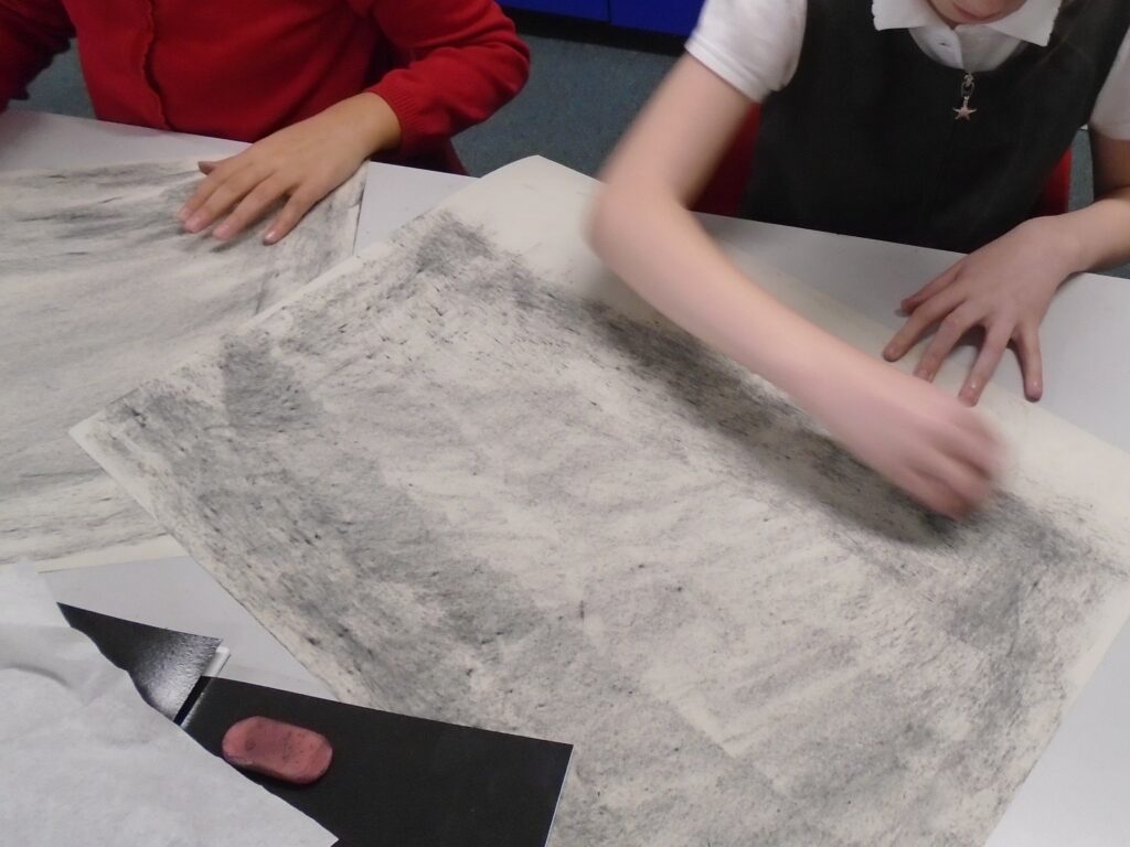 Using charcoal to cover a large piece of paper.