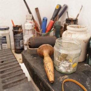 Jam jars holding paint brushes and other printmaking materials.