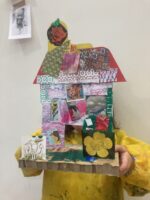A girl holding up her cardboard autobiographical house model.