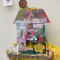 A girl holding up her cardboard autobiographical house model.